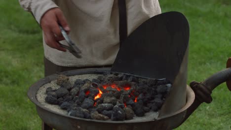 A-revolutionary-war-reinacter-blacksmith-puts-a-piece-of-metal-in-hot-coals-to-heat-up-while-he-pumps-the-bellows