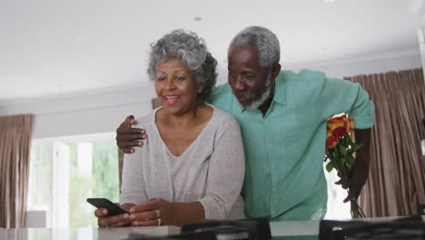 a senior african american man offering flowers to his wife. social distancing in quarantine.