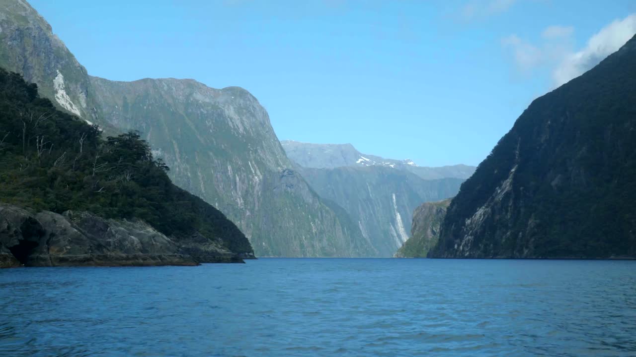 A beautiful view of a deep blue fjord surrounded by towering, green-clad mountains under a clear blue sky.
