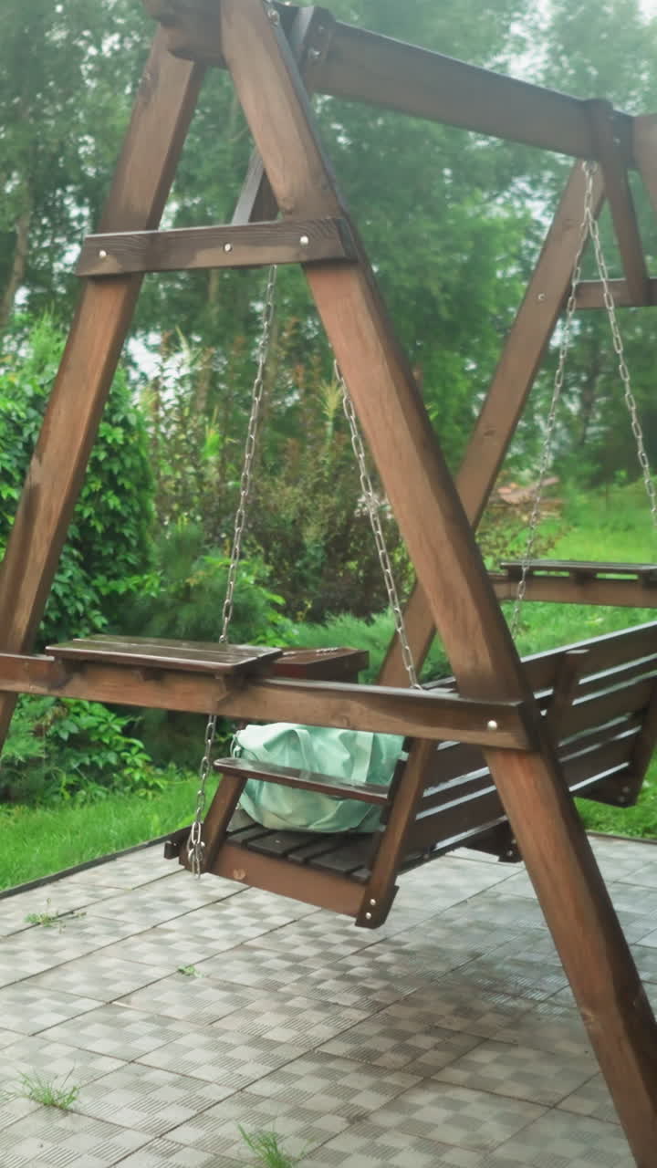 물로 가득 찬 플라스틱 물 드럼과 색 가방을 들고 있는 야외 목조 스 벤치, 배경에는 초록색, 꽃, 나무가 있는 울창한 정원이 있습니다.