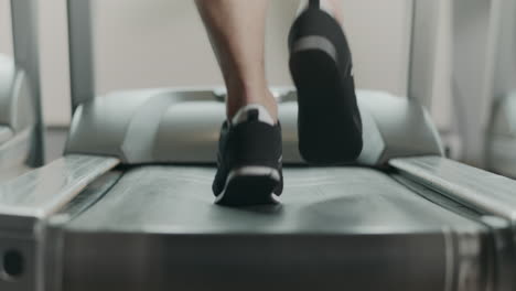 Closeup-feet-starting-run-on-treadmill-in-fitness-gym.-Back-view-of-black-shoes