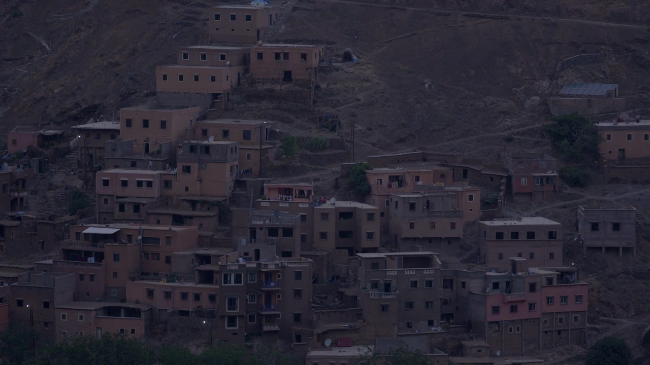 Vista cinematografica dall'alto di un tradizionale villaggio berbero costruito tra le scogliere rocciose delle montagne dell'Atlante in Marocco, che mostra l'architettura in mattoni di fango con tetti piatti durante la quiete dell'alba