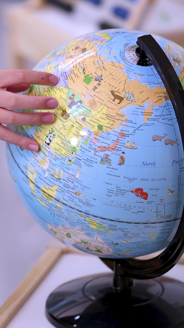 Várias crianças giram e tocam um globo terrestre brilhante de sala de aula sob iluminação interna suave.