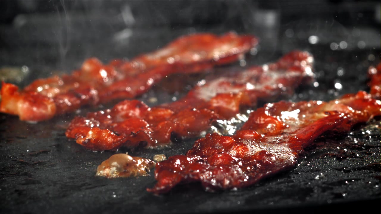 Bacon croccante che frigge con grasso sfrigolante su una piastra calda