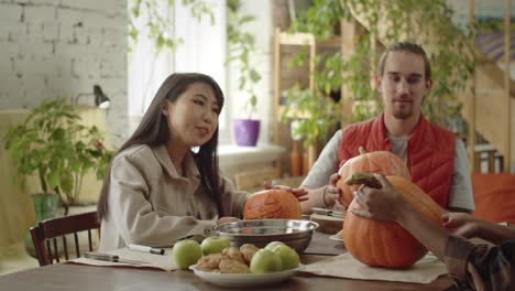 friends are sitting at the table and discussing how to carve their halloween pumpkins