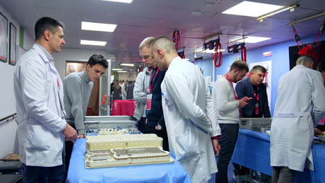 students' group stands at the table with modern medical tools. male educator in white robe answers questions.