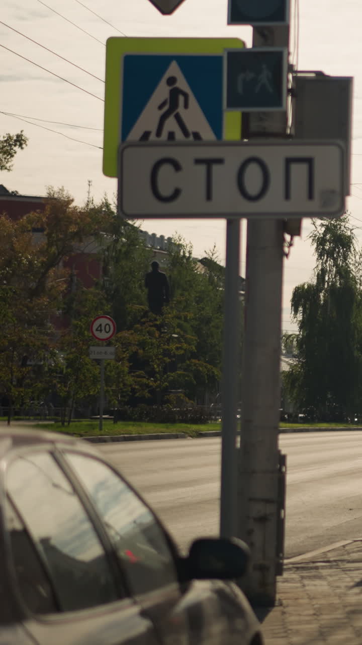 paso de peatones junto a una señal de stop, coche aparcado en el borde de la acera y señal de peatones montada en un poste, luz del sol al final de la tarde proyectando largas sombras, un viajero solitario cruza la calle, intersección urbana tranquila