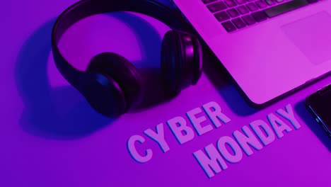 composition of laptop, headphones and smartphone with cyber monday text on purple background