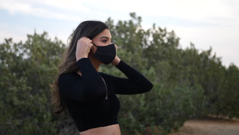 Adult-hispanic-woman-putting-on-a-reusable-cloth-respiratory-face-mask-to-prevent-disease-from-the-corona-virus-while-social-distancing-in-quarantine-during-the-pandemic