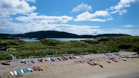 a rising 4k drone shot of derrynane caherdaniel beach with colourful kayaks and mountains in the backdrop