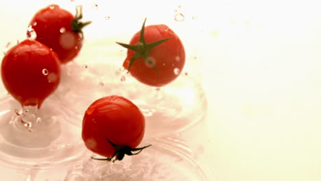 cherry tomatoes falling on white wet surface