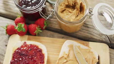 sándwich de mantequilla de maní y jalea en una bandeja de madera con leche y fresas en una superficie de madera