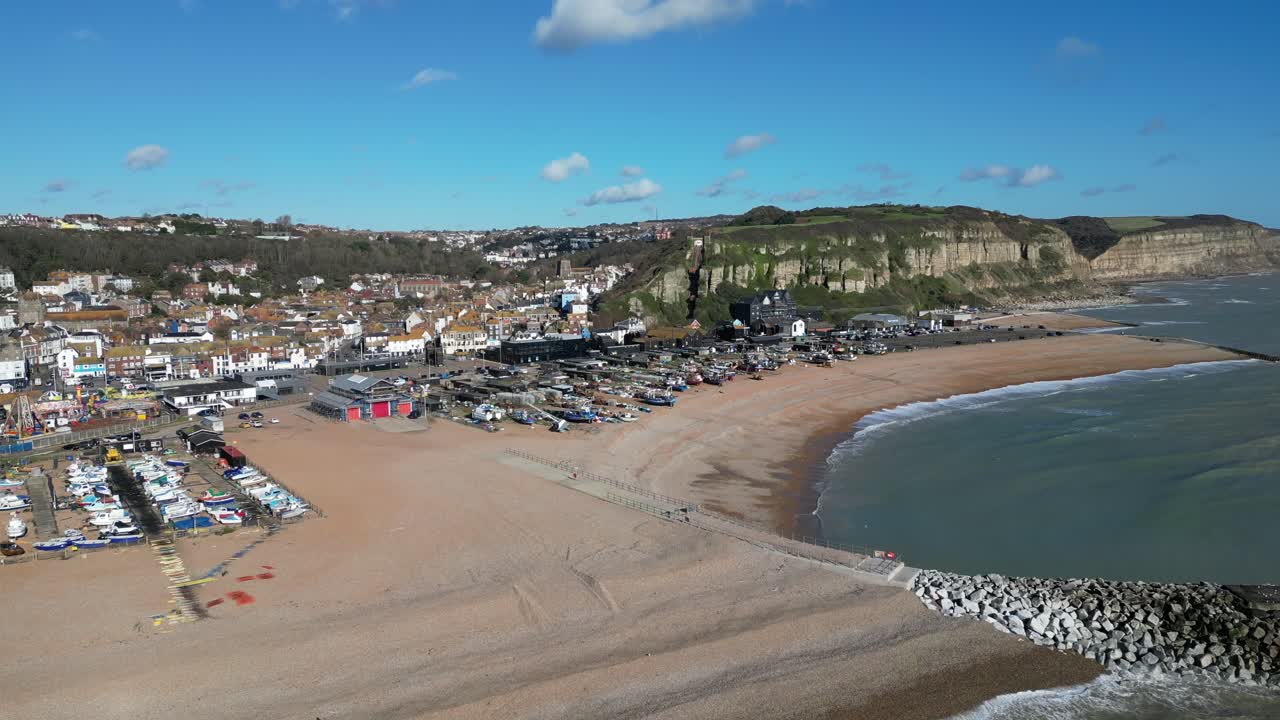 Tomada aérea de drone de Hastings, Reino Unido, filmagem em órbita alta da frota de pesca costeira da praia, da Cidade Velha e das Falésias de East Hill.