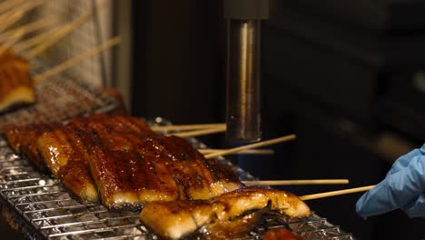 a chef uses a blowtorch to caramelize skewered meat, achieving a glossy finish on a metal grill.