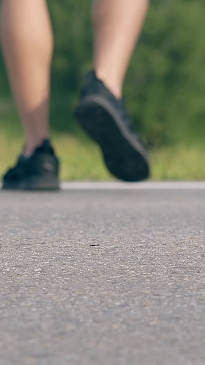 young couple in skaters walks on gray road near white falling sling by green field low angle backside shot slow motion