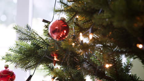 Rack-Fokus-Nahaufnahme-Von-Glitzernden-Kugeln,-Die-An-Einem-Weihnachtsbaum-Mit-Lichterketten-Und-Bokeh-Hängen