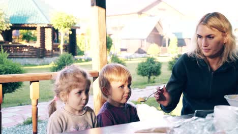 travelling young pretty mother feeds children they are sitting in a summer house