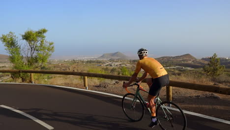 tracking video shot of a male cyclist climbing up a mountain road. man doing cycling training on a hilly highway road on a sunny day.