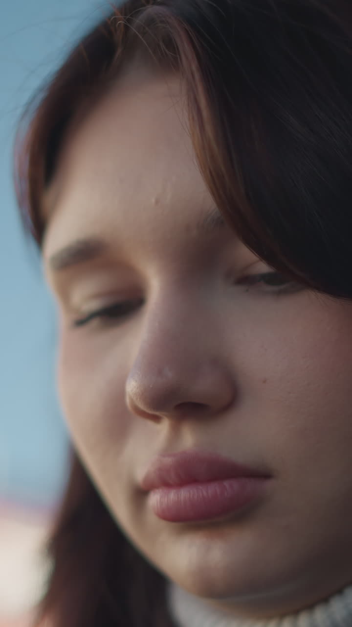 primer plano de una mujer joven con labios rosados, ojos ligeramente caídos y anillo en la nariz, enfocando con expresión reflexiva, iluminación suave, mirada tranquila y serena, con fondo borroso