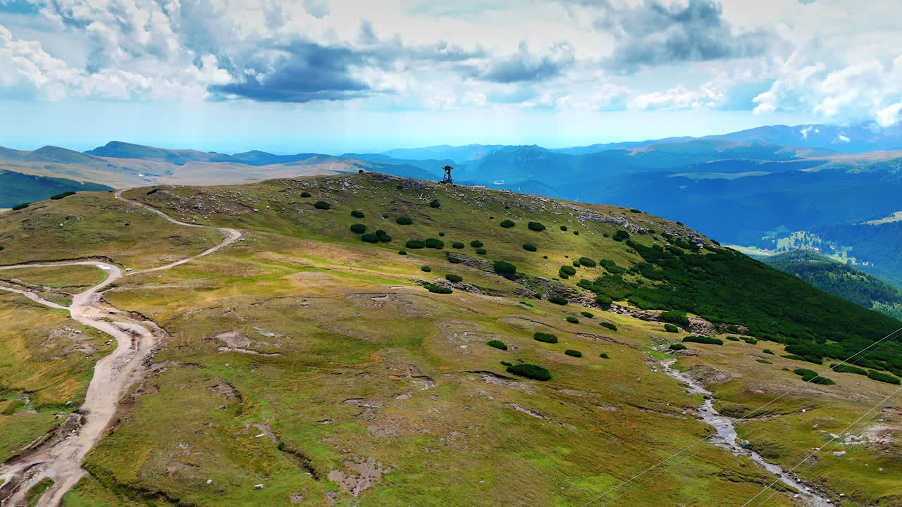 Mountains with distant building. A vast green landscape under a blue sky showcases rolling hills and a distant tower on a mountain ridge