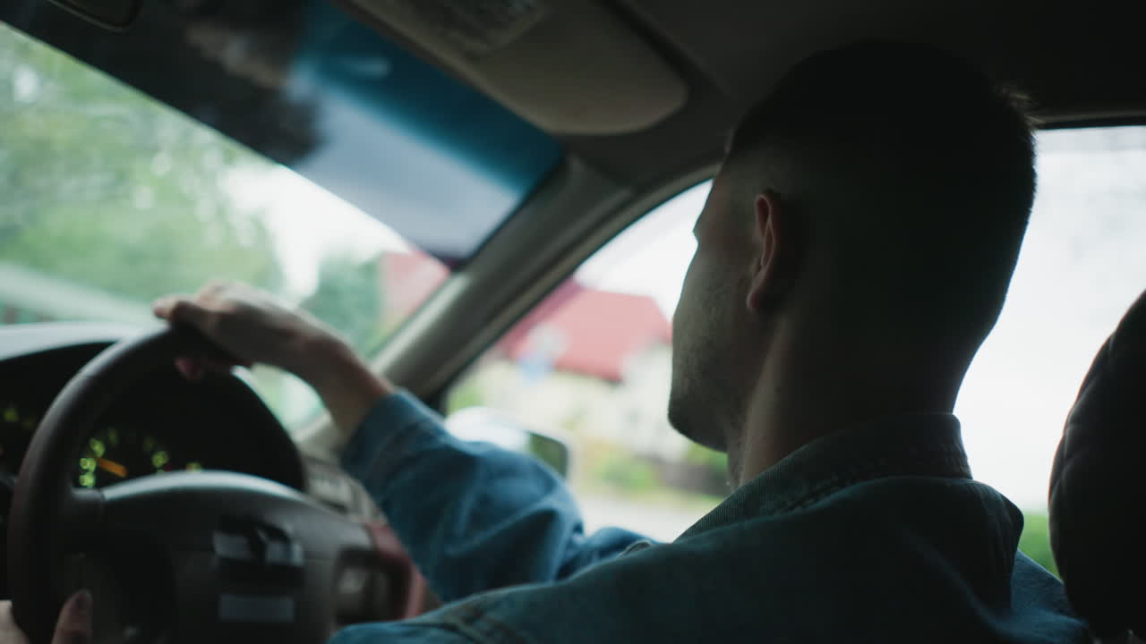 man driving car through forest road, denim jacket profile, moody interior lighting, thoughtful gaze on winding lane, close view of steering and dashboard, calm cinematic atmosphere