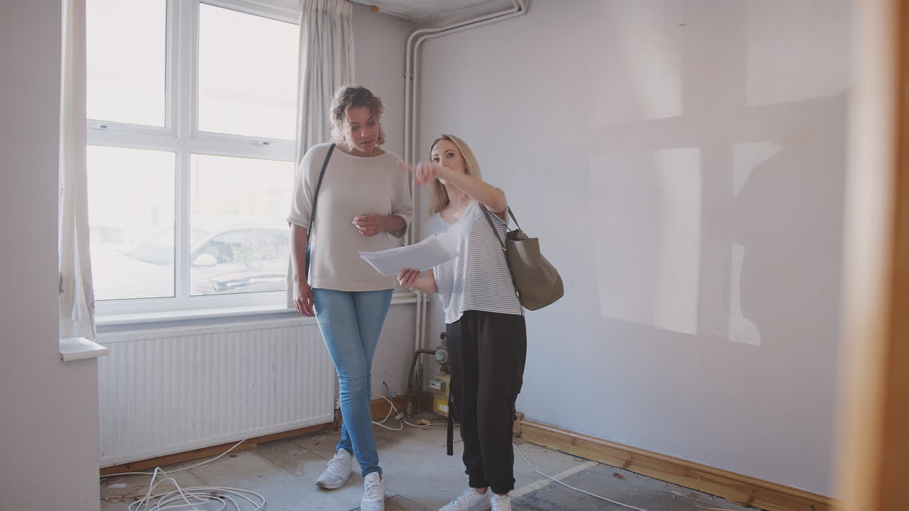 Two Female Friends Buying House For First Time Looking At House Survey In Room To Be Renovated
