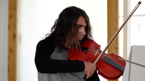 Ethnic-male-musician-in-grey-and-black-long-sleeve-shirt-performing-long-bow-strokes-on-red-viola-in-white-studio