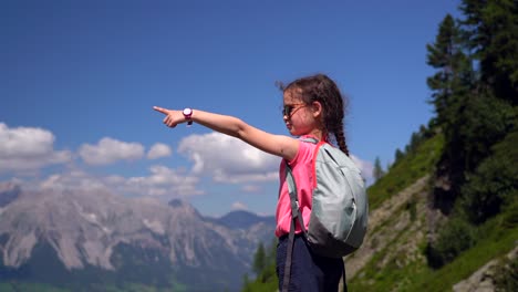 girl hiking on beautiful summer day in alps mountains austria, resting on rock and admire amazing view to mountain peaks. active family vacation leisure with kids. outdoor fun and healthy activity