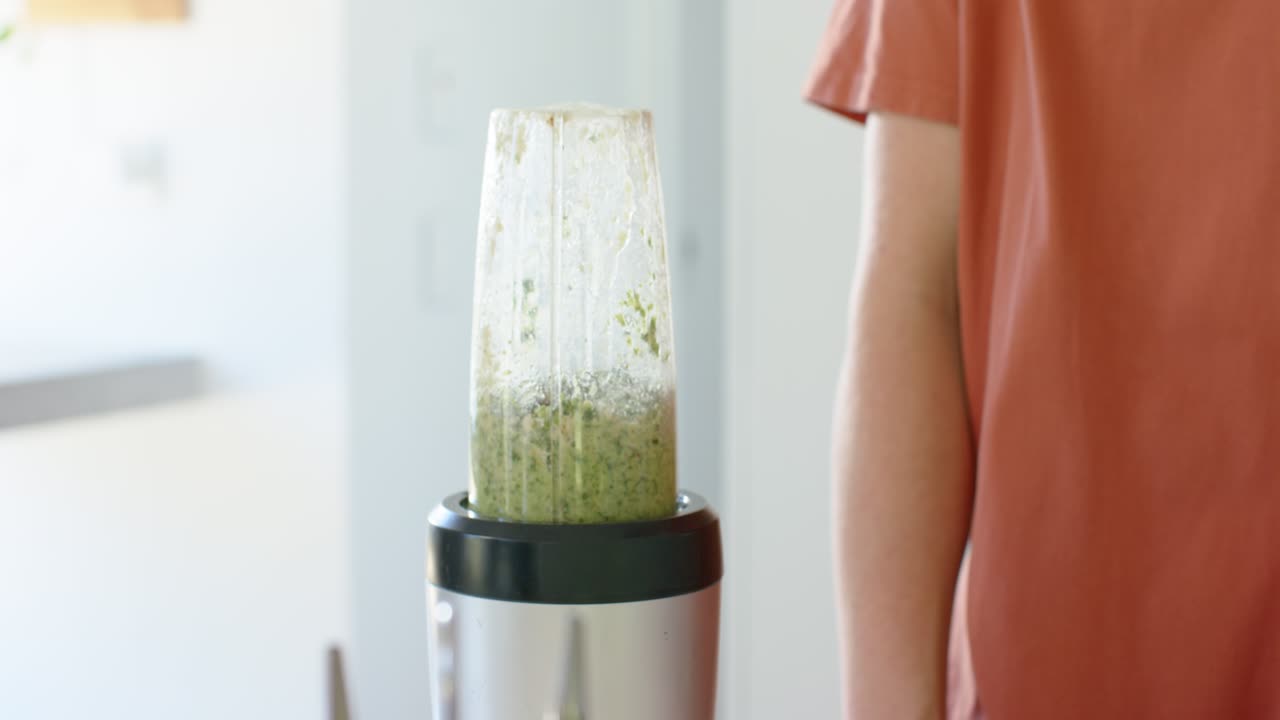 Kompakt blender er i drift på kjøkkenbenken etter å ha blitt slått på, blander grønn smoothie for servering.