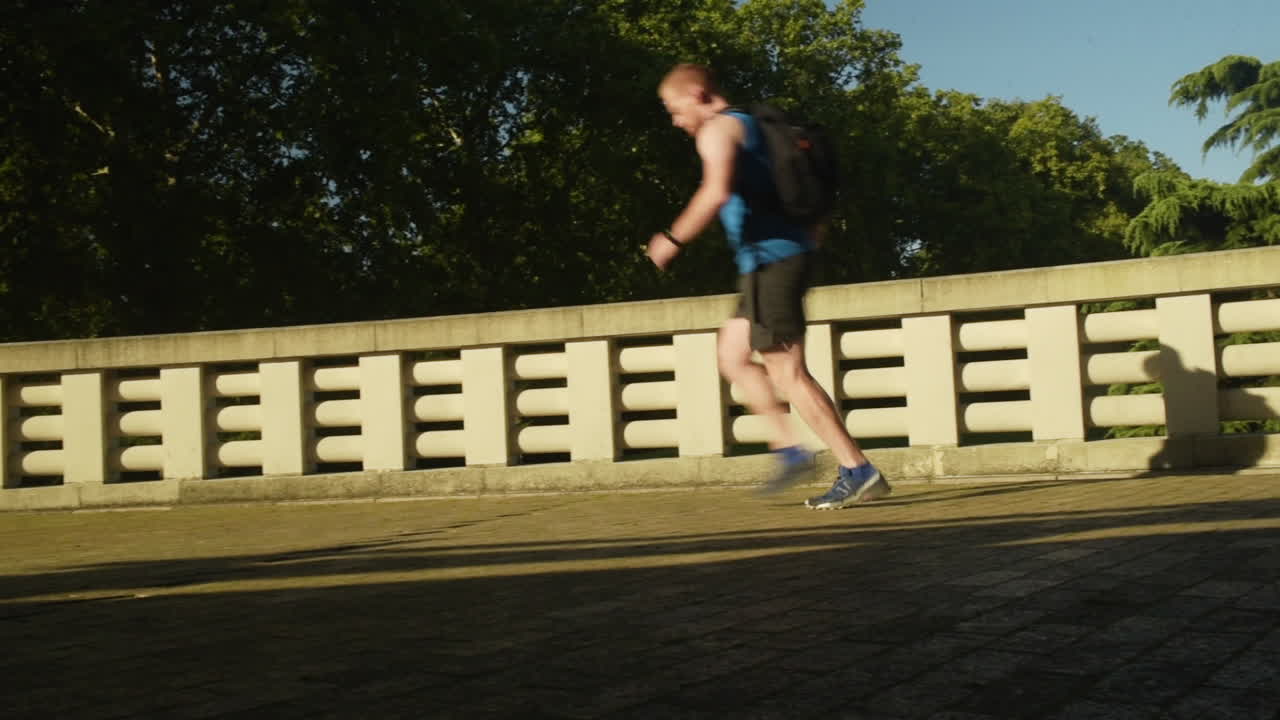 A fit man runs down the last light of the sun as it sets casting dark shadows contrasting against the decorated wall in the Battersea Park
