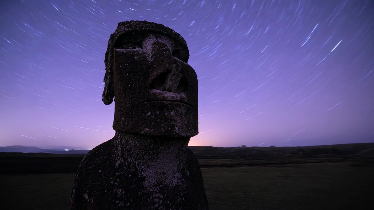 Ripresa notturna in timelapse: telecamera filma moai ricoperti di licheni con panoramica frontale, registrando scie stellari sul campo.