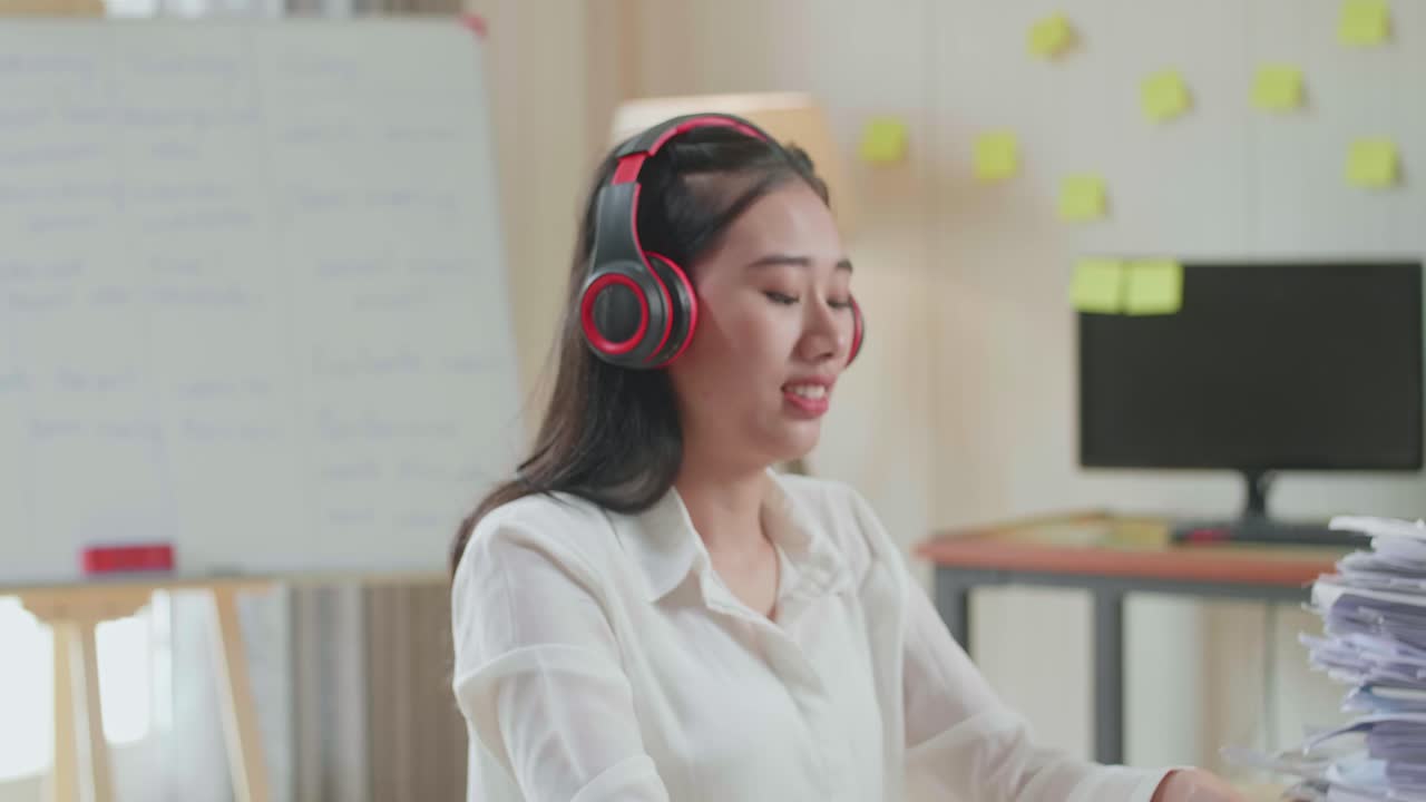 사무실에서 문서 작업을 한 후 스마트폰에서 음악을 듣는 헤드폰을 가진 아시아 여성의 클로즈업