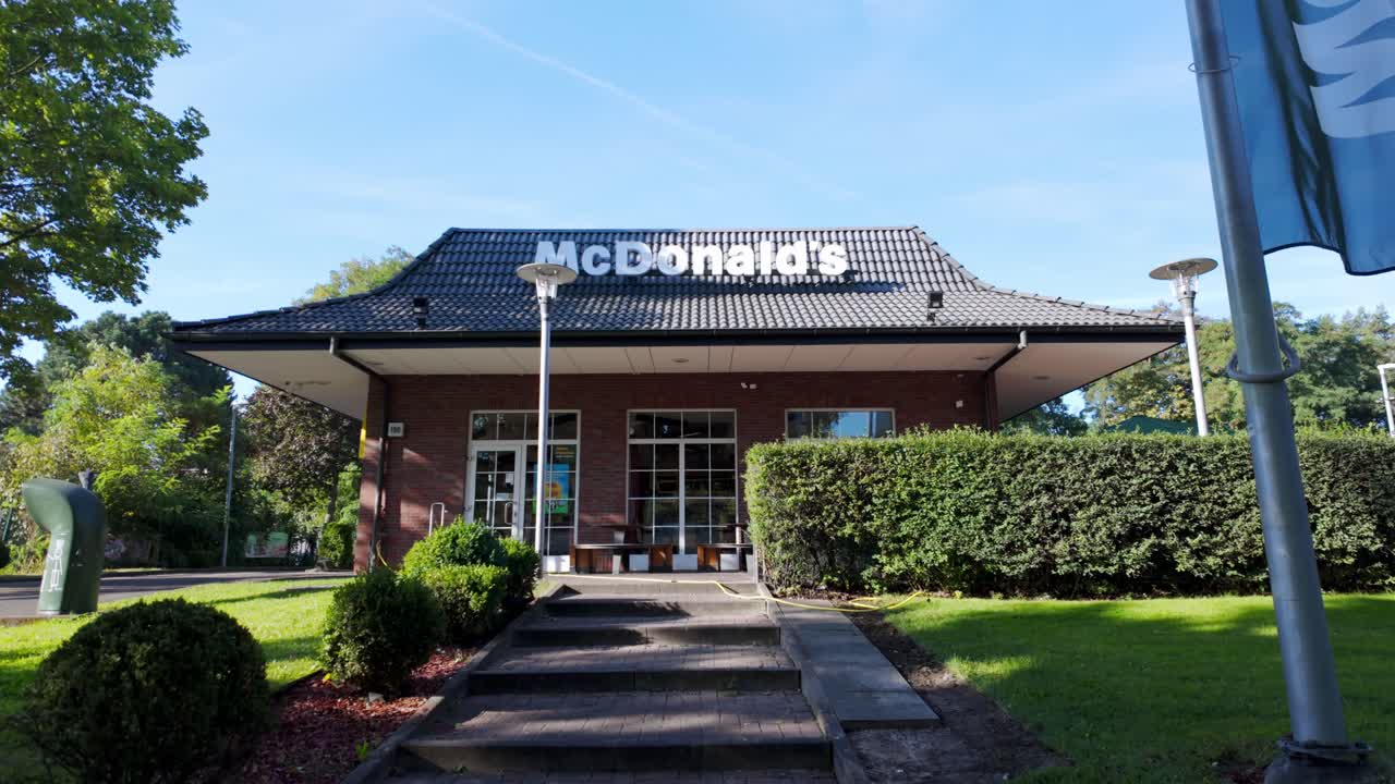 This video showcases the exterior of a McDonald's in Berlin, filmed with a smooth tilt-down camera movement, capturing the iconic branding and lush surroundings