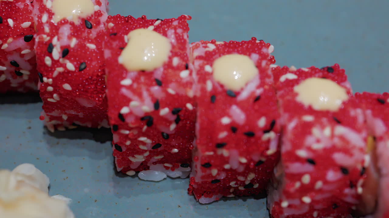 Close up of vibrant red sushi rolls topped with creamy sauce and sesame seeds, served on a ceramic plate
