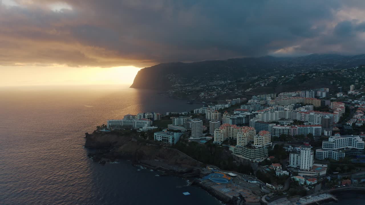 Pôr do sol aéreo sobre o Funchal, Madeira, com hotéis e o oceano.