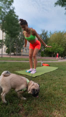 woman practicing yoga in a park with a pug