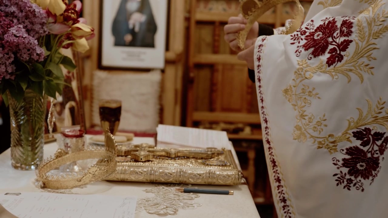 Filmový detailní záběr pravoslavného kněze provádějícího tradiční náboženský rituál uvnitř východního pravoslavného chrámu. Scéna zahrnuje zdobené liturgické oděvy a zlaté náboženské předměty.