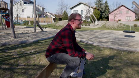 happy young man jumps over bench in park and sits, smiling person in medium shot