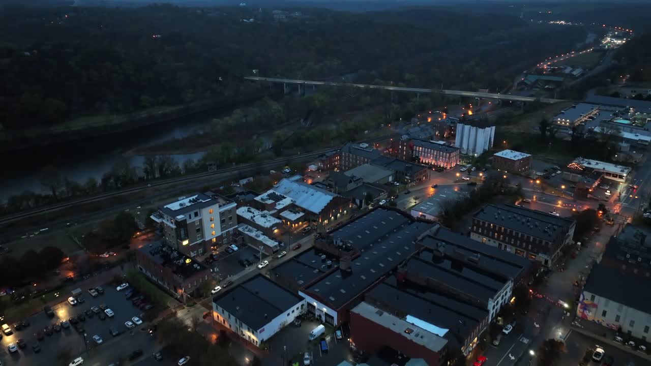 Aerial flyover housing area of small city in Virginia with driving cars on bridge. Dark night in suburb with lighting lantern along street. Railroad with tracks. Wide shot.
