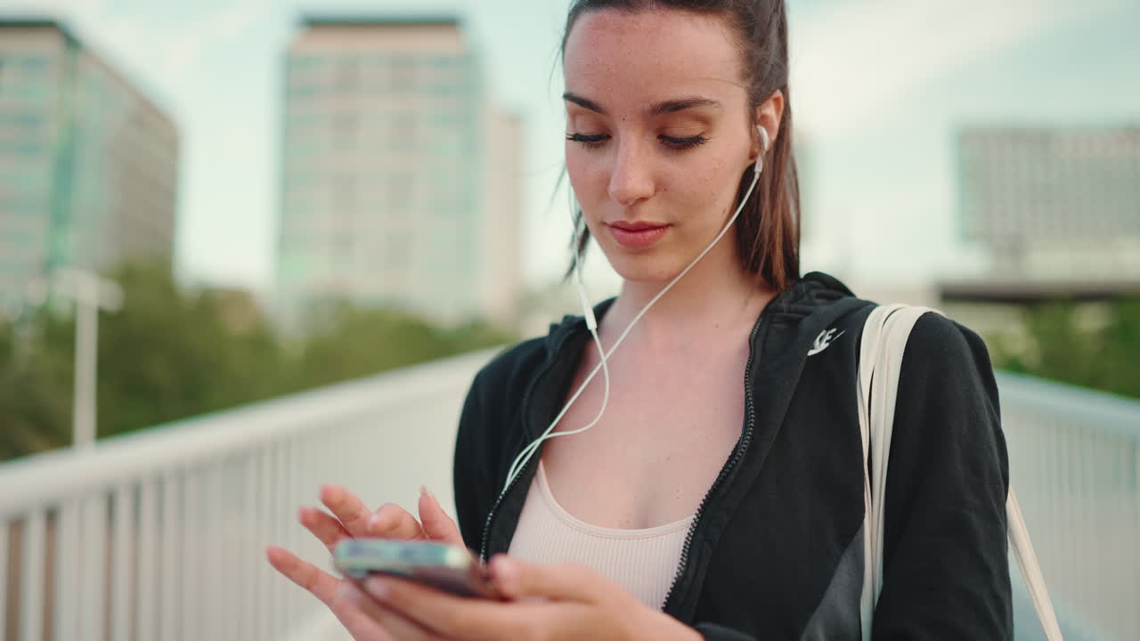 Giovane donna con smartphone e auricolari su un ponte cittadino