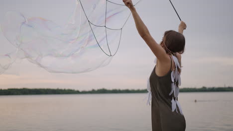 a young girl artist shows magic tricks using huge soap bubbles. create soap bubbles using sticks and rope at sunset to show a theatrical circus show