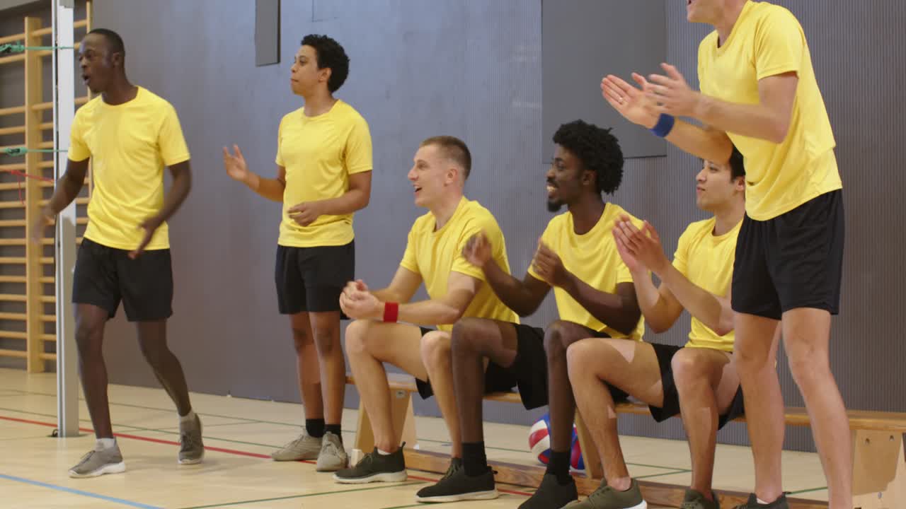 Männerteam in gelben Trikots reagiert auf Spielzug links, klatscht, unterstützt von der Bank, Volleyball in der Sporthalle.