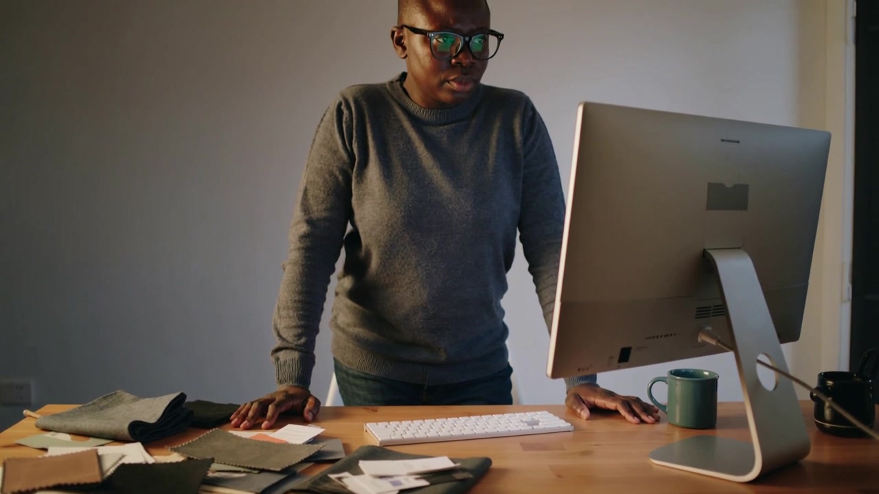 Premendo i palmi, un designer in maglione in studio confronta campioni di tessuto con il monitor per abbinare i colori.