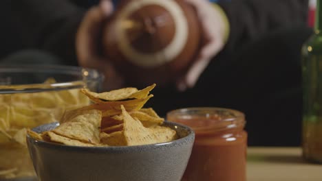 Person-Zu-Hause,-Die-Ein-American-Football-Spiel-Im-Fernsehen-Mit-Getränken,-Snacks-Und-Ball-Sieht-4