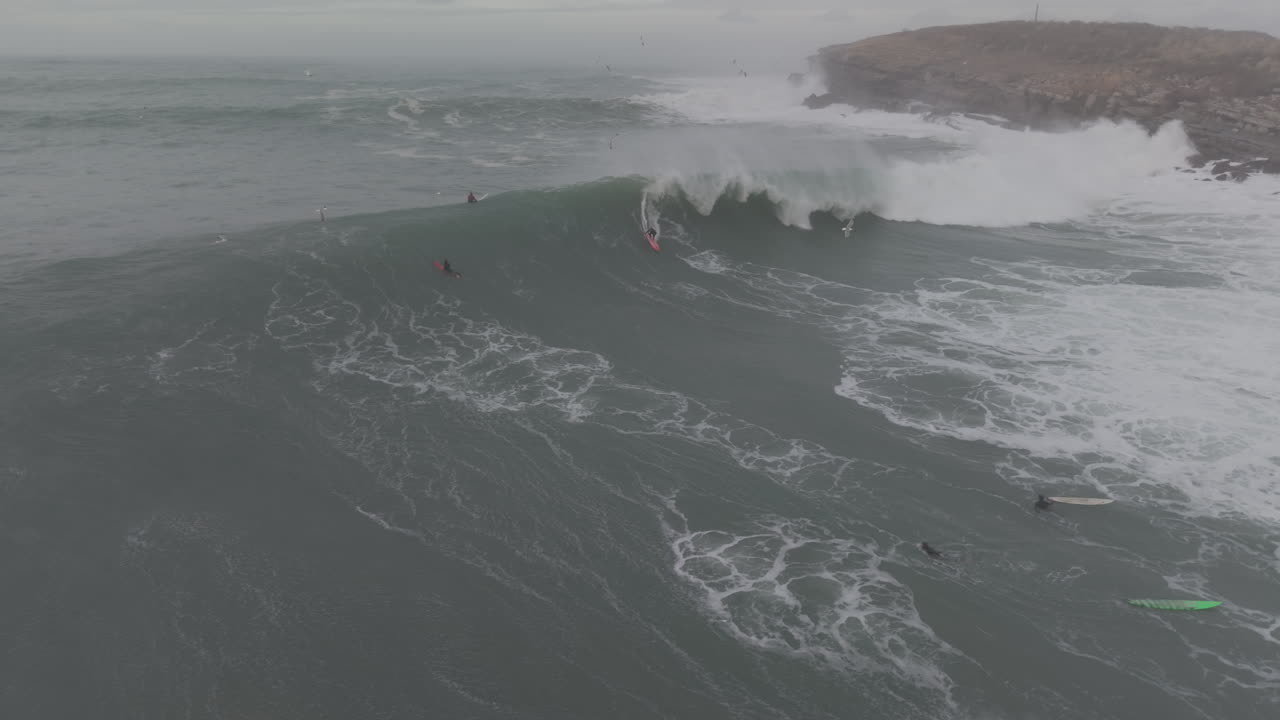 Luftfoto af surfer, der rider på en massiv havbølge nær klippekysten