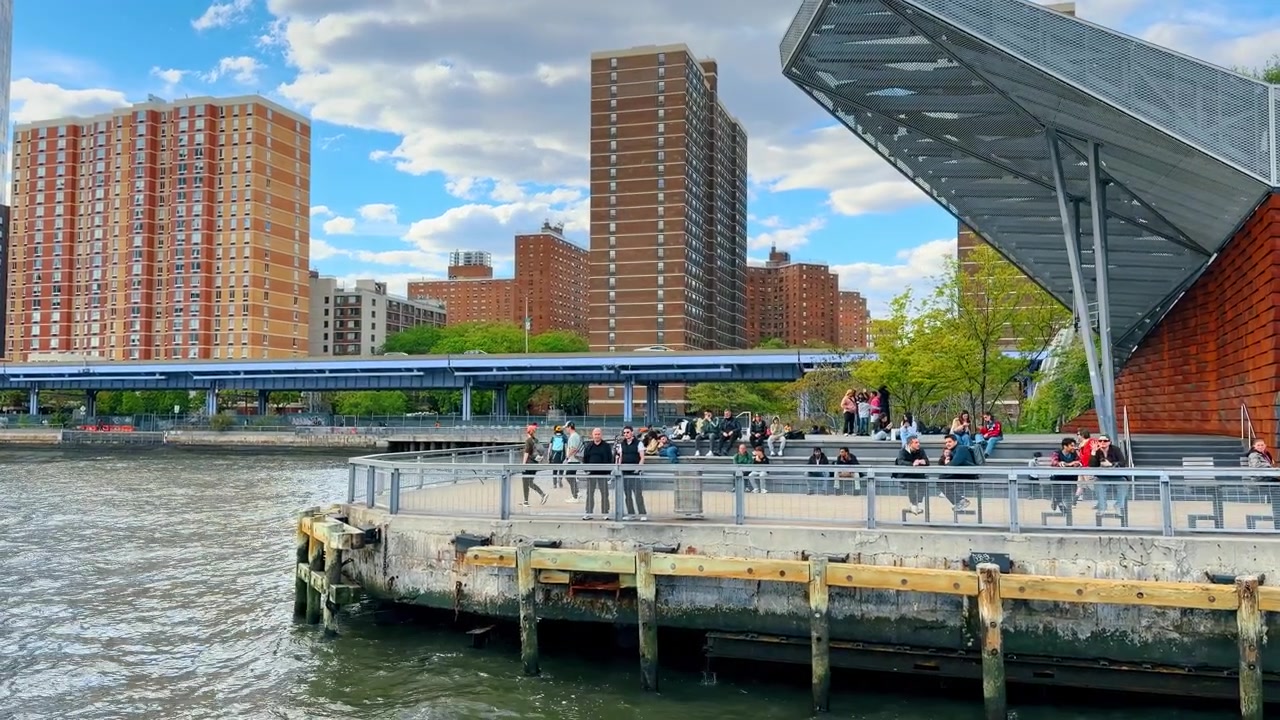 New York, États-Unis, 22 mai 2026 : Quai riverain et promenade le long de l'East River à New York. Des gens assis sur un ponton public moderne près de l'East River avec des bâtiments résidentiels urbains en arrière-plan.