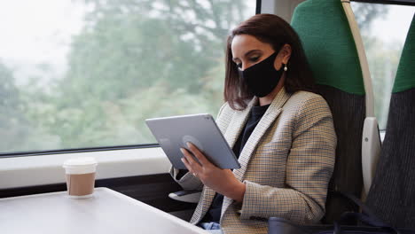 businesswoman on train using digital tablet wearing ppe face mask during health pandemic