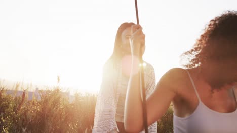 feliz pareja romántica de lesbianas biraciales jugando en el columpio en el jardín al atardecer, cámara lenta