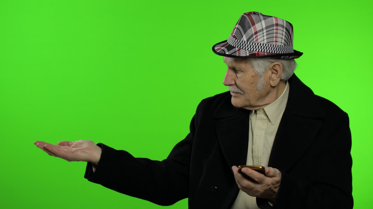 Elderly caucasian grandfather using smartphone, pointing at something with hand