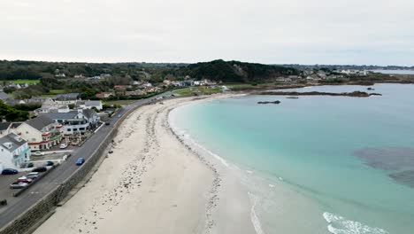 Cobo-Bay-Guernsey-flight-over-golden-beach-crystal-clear-sea-rocks-and-seafront-including-The-Rockmount-and-Cobo-Bay-Hotel-on-calm-sunny-day